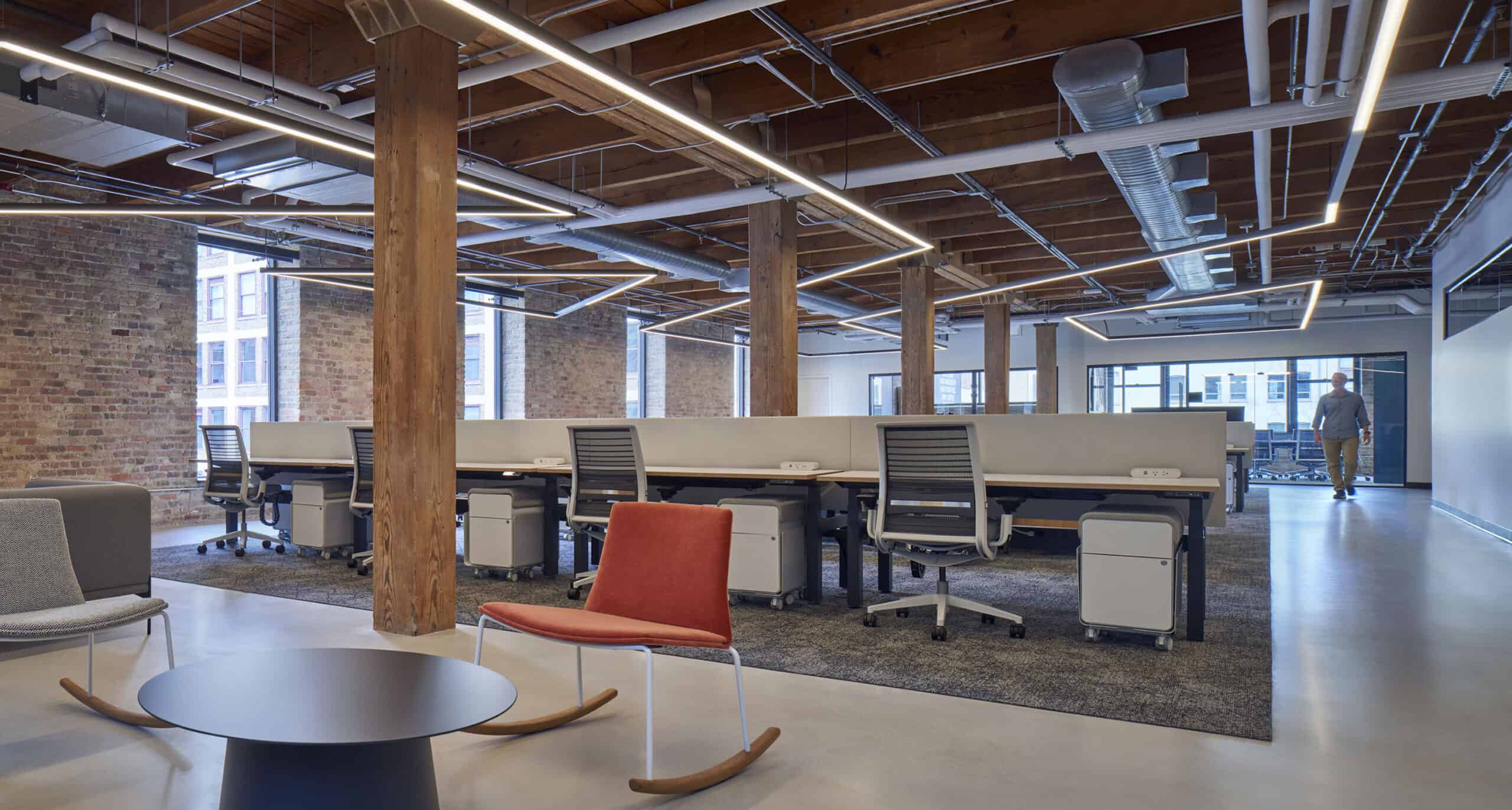 Open office with coworking and lounge area and cubicles for individual work. Red rocking chair and office chairs. 