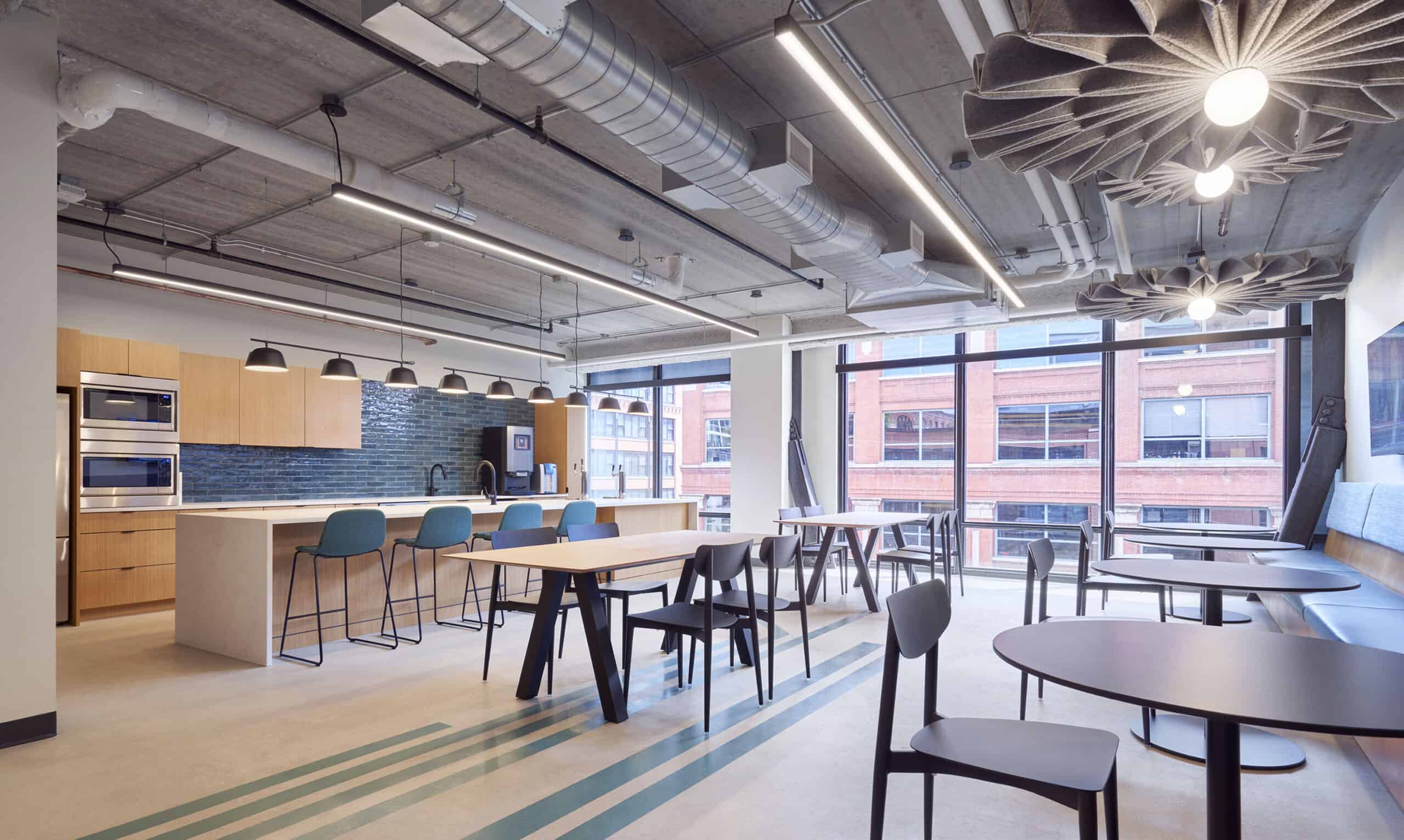 Modern open kitchen in a commercial office with blue tile, blue barstools, and plenty of tables for coworking and eating. 